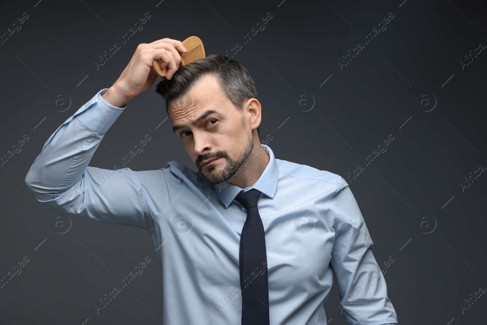 Photo of Handsome man combing his hair on dark background