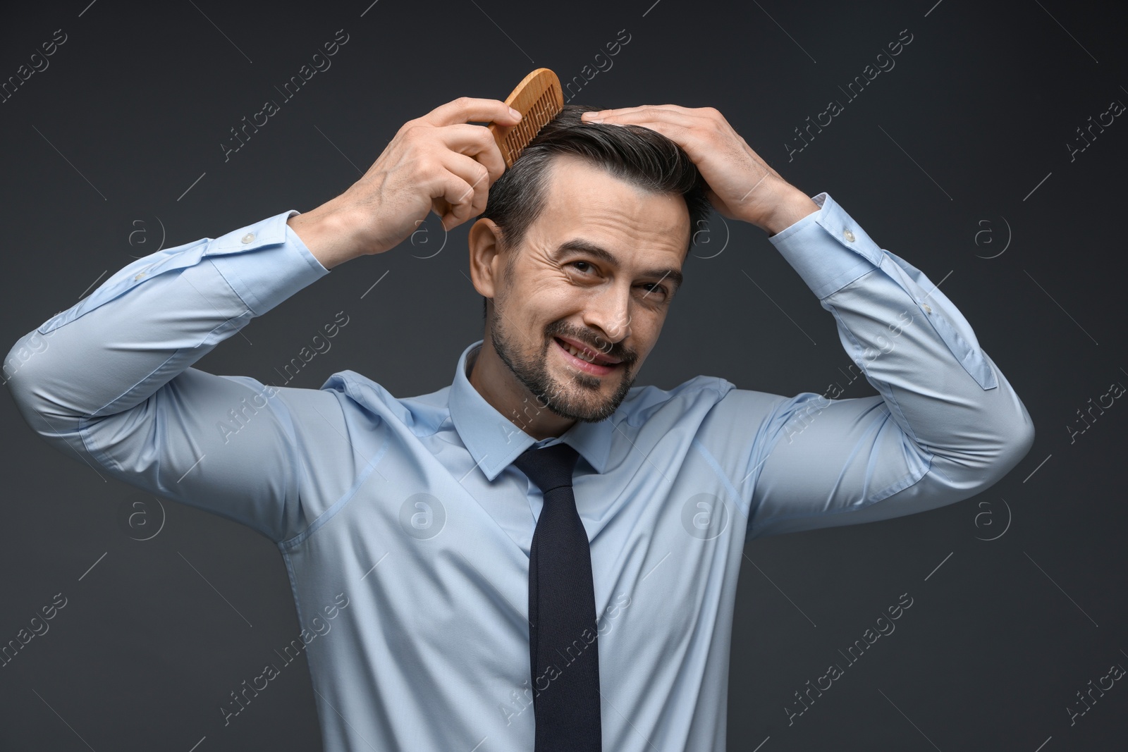 Photo of Handsome man combing his hair on dark background