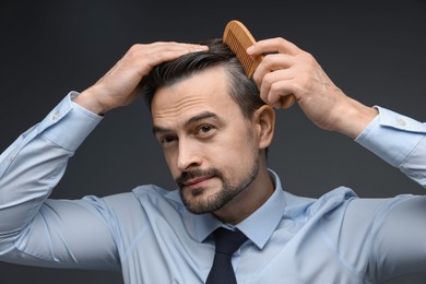 Photo of Handsome man combing his hair on dark background