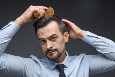 Photo of Handsome man combing his hair on dark background