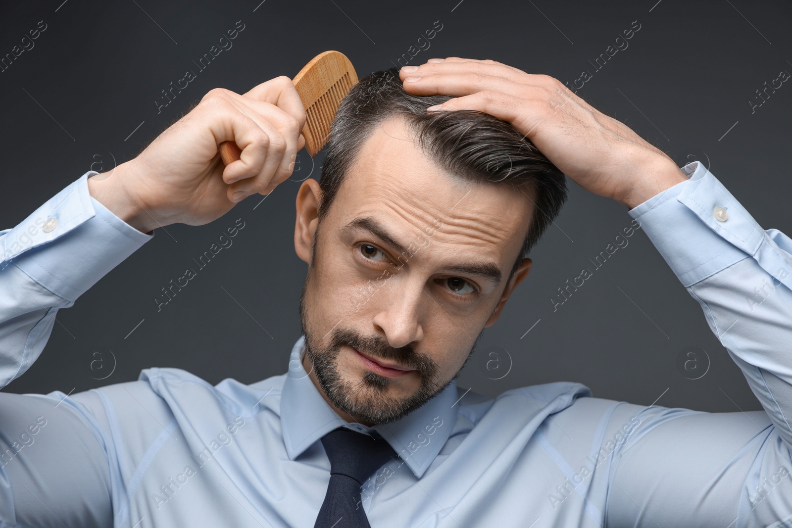 Photo of Handsome man combing his hair on dark background