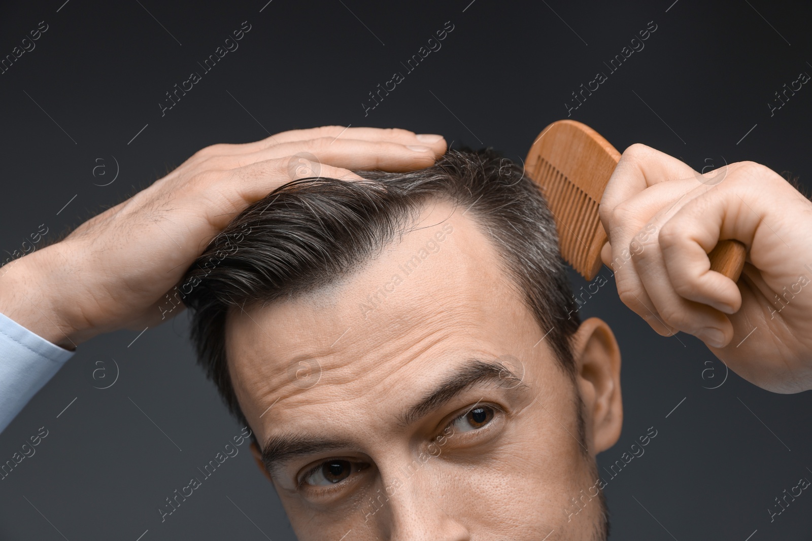 Photo of Handsome man combing his hair on dark background, closeup