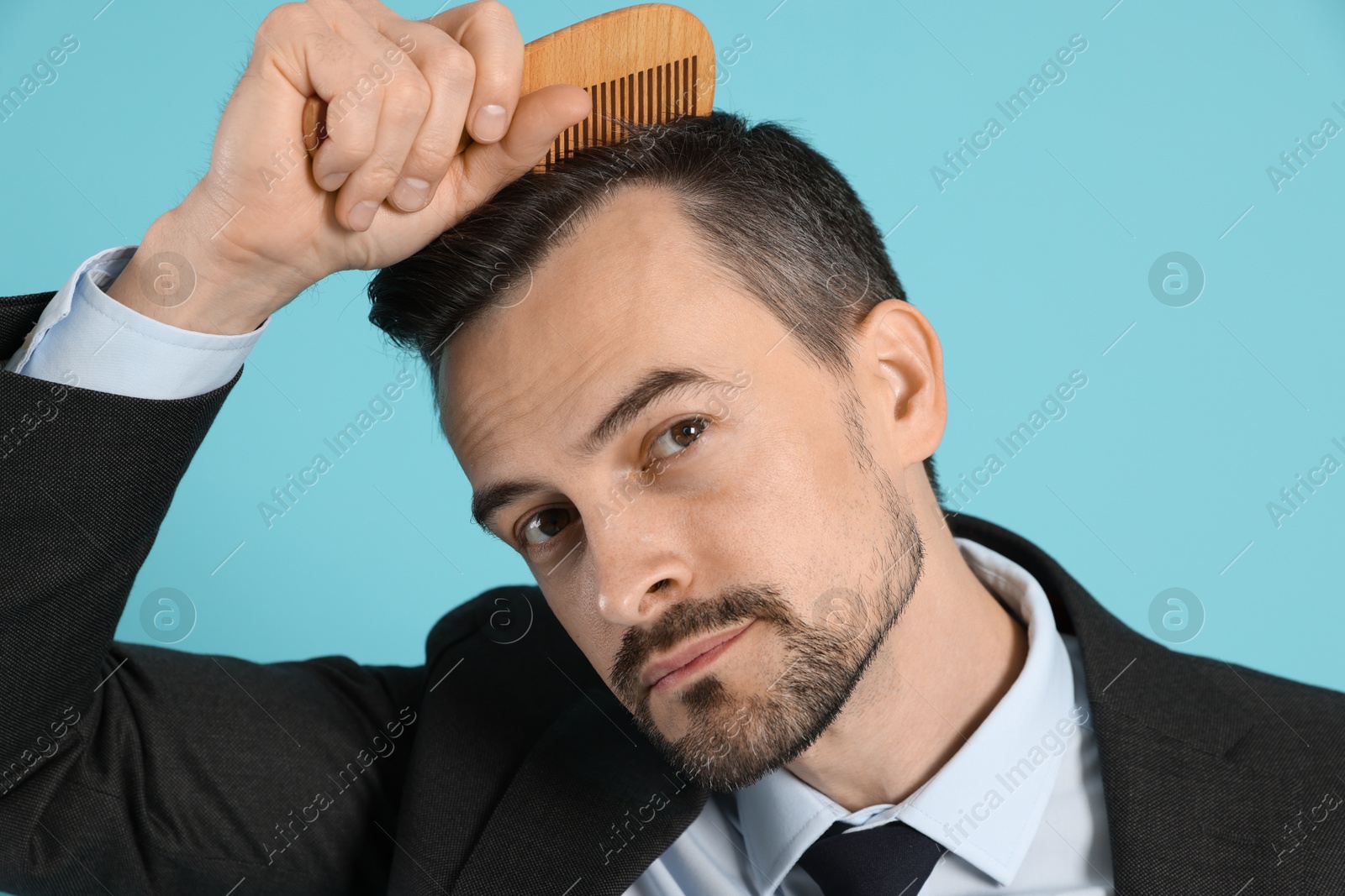 Photo of Handsome man stylish his hair with comb on light blue background