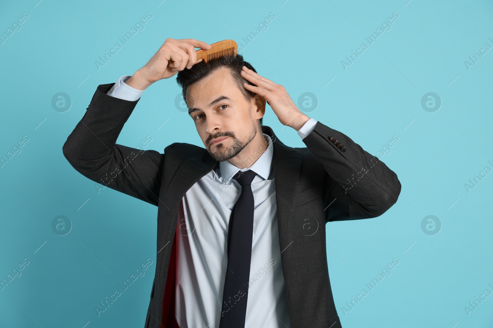 Photo of Handsome man stylish his hair with comb on light blue background