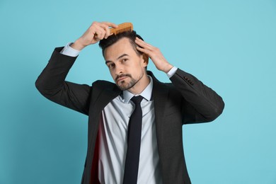 Handsome man stylish his hair with comb on light blue background