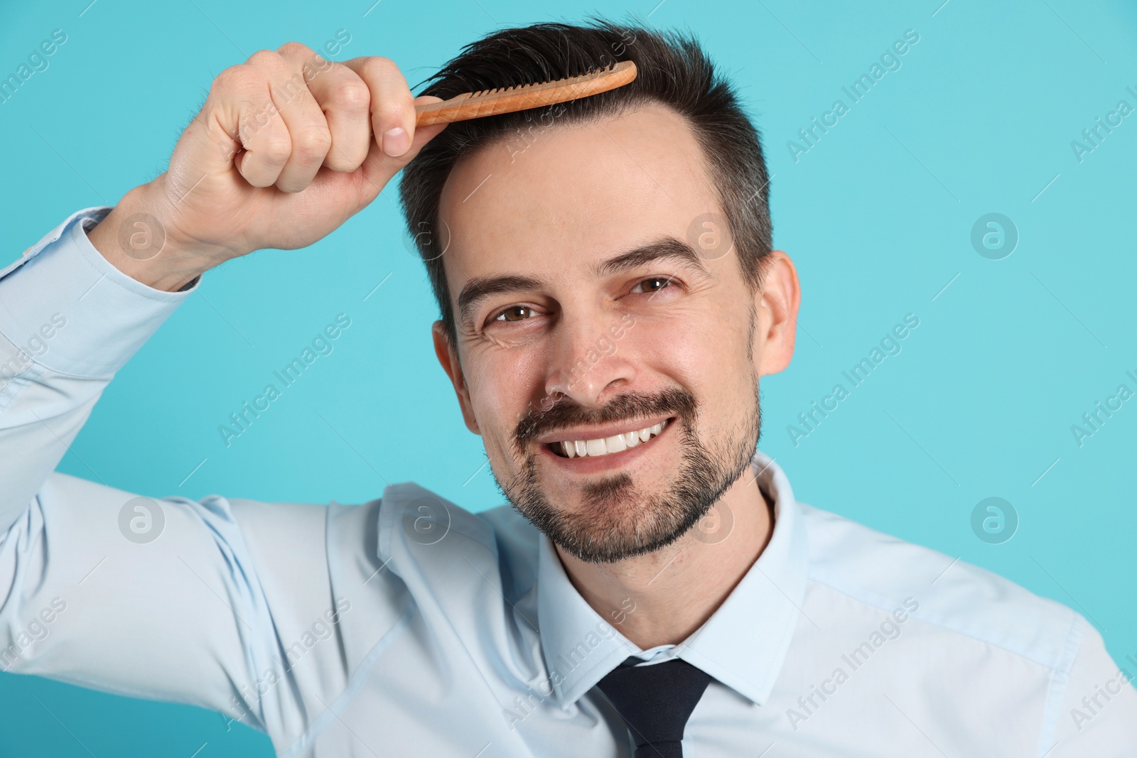 Photo of Handsome man stylish his hair with comb on light blue background