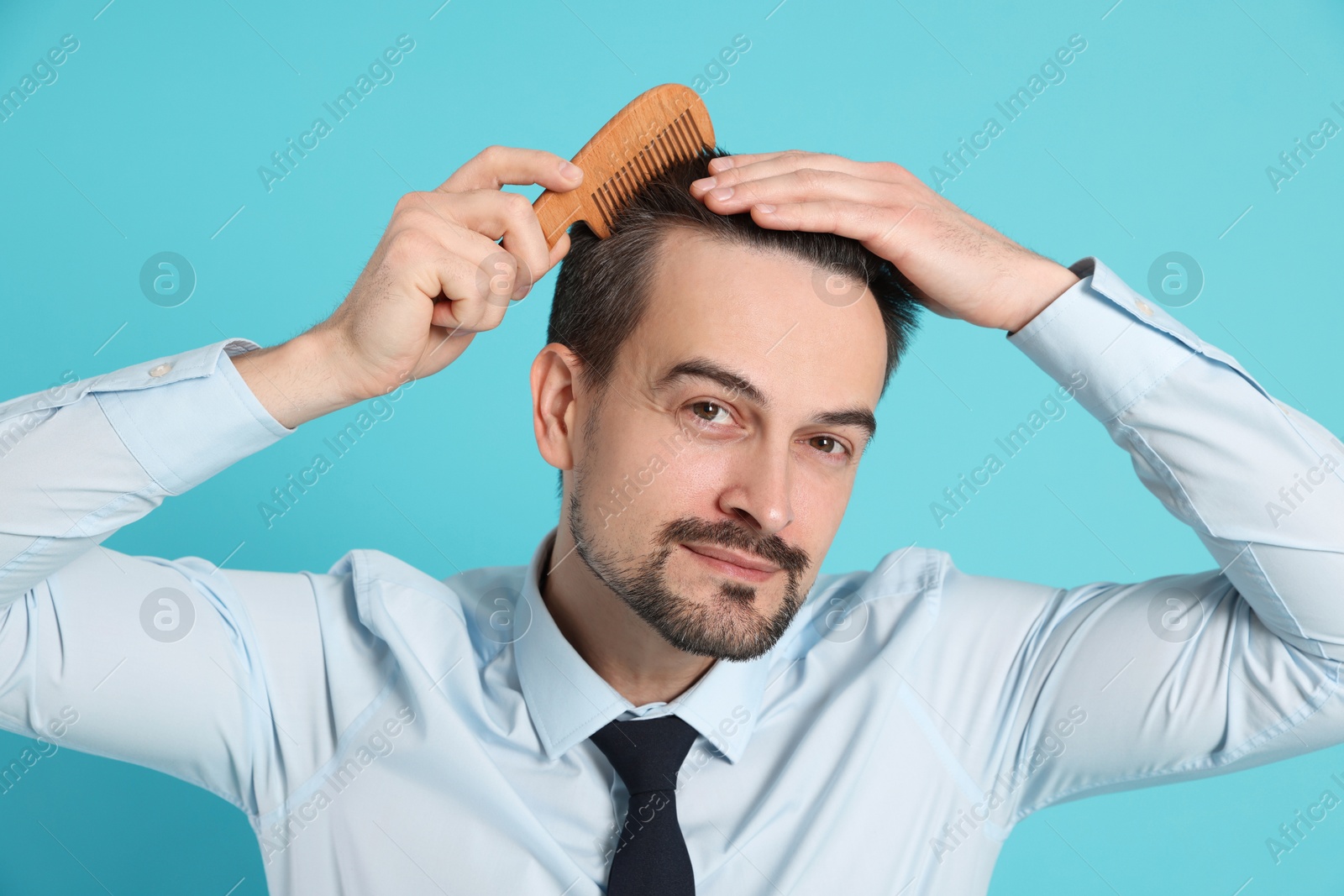 Photo of Handsome man stylish his hair with comb on light blue background