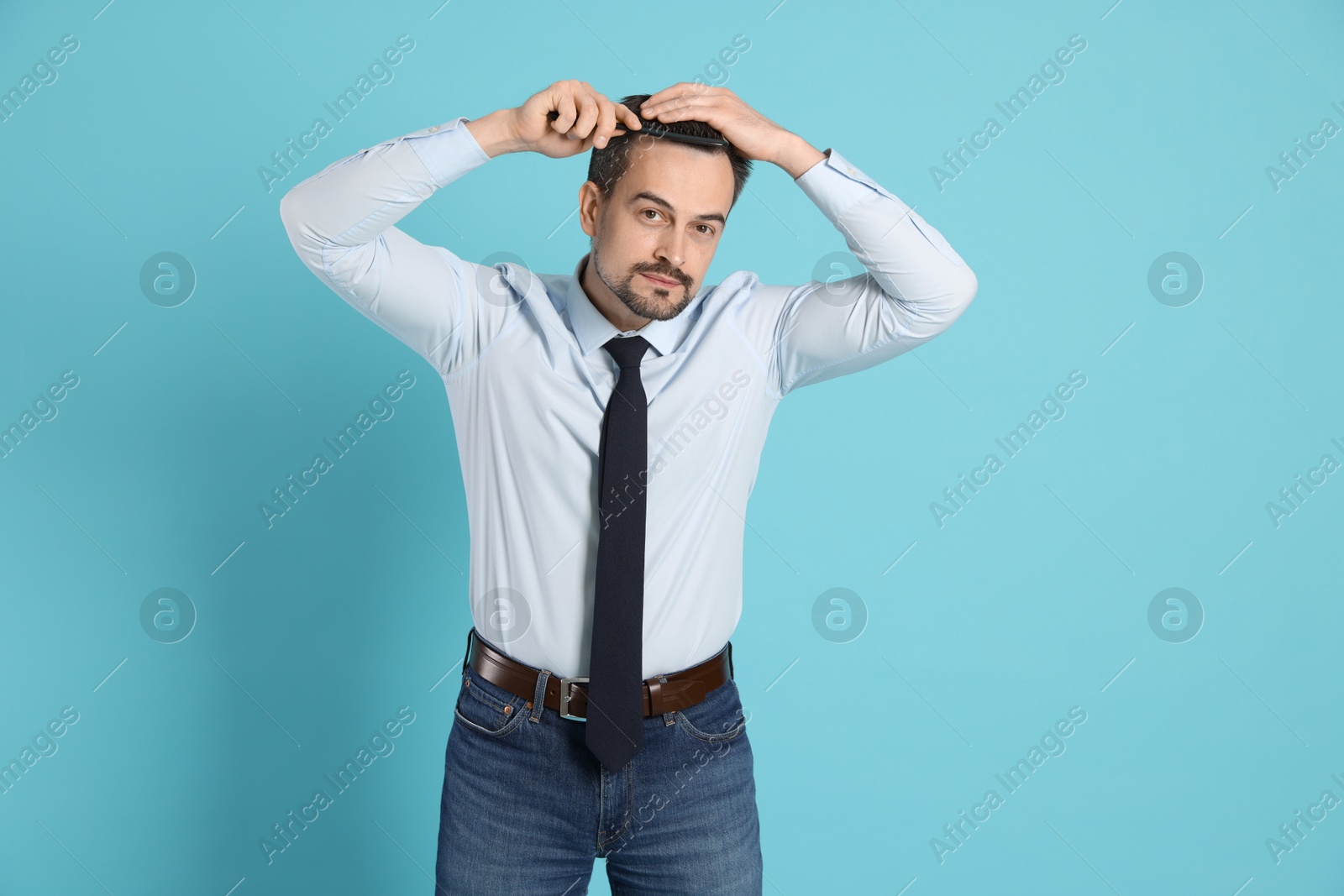 Photo of Handsome man stylish his hair with comb on light blue background