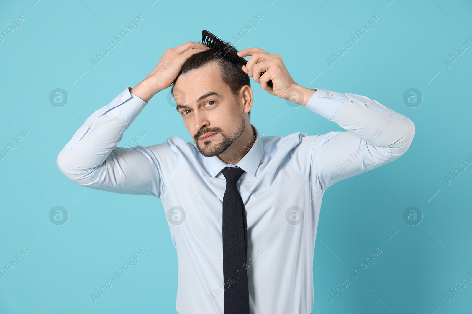 Photo of Handsome man stylish his hair with comb on light blue background