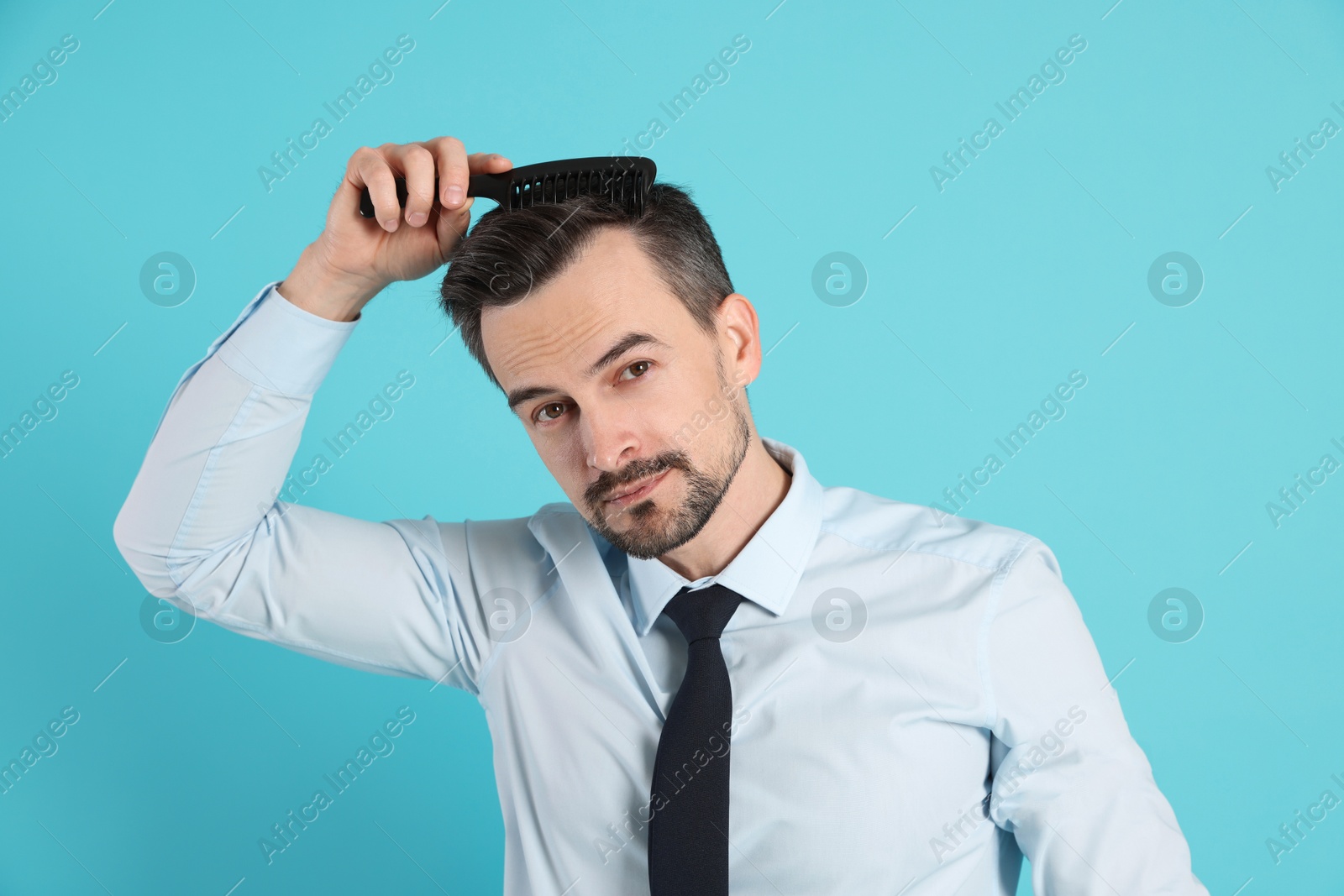 Photo of Handsome man stylish his hair with comb on light blue background