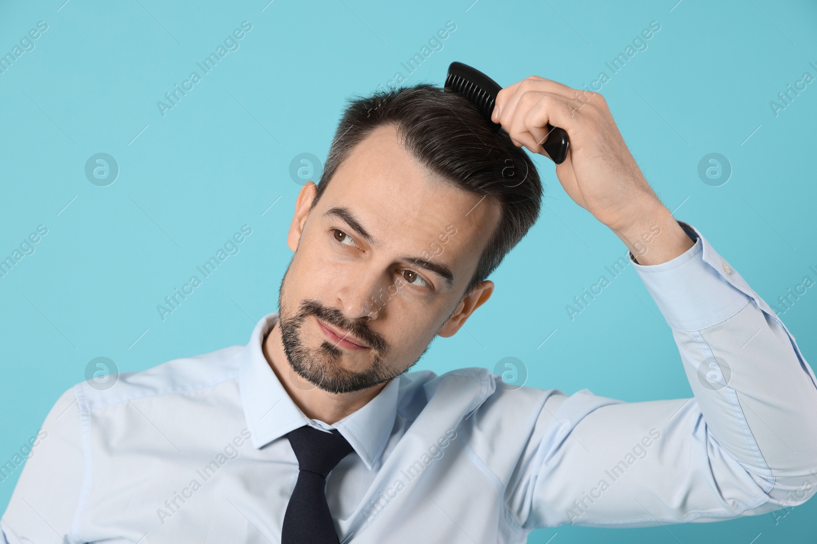 Photo of Handsome man stylish his hair with comb on light blue background