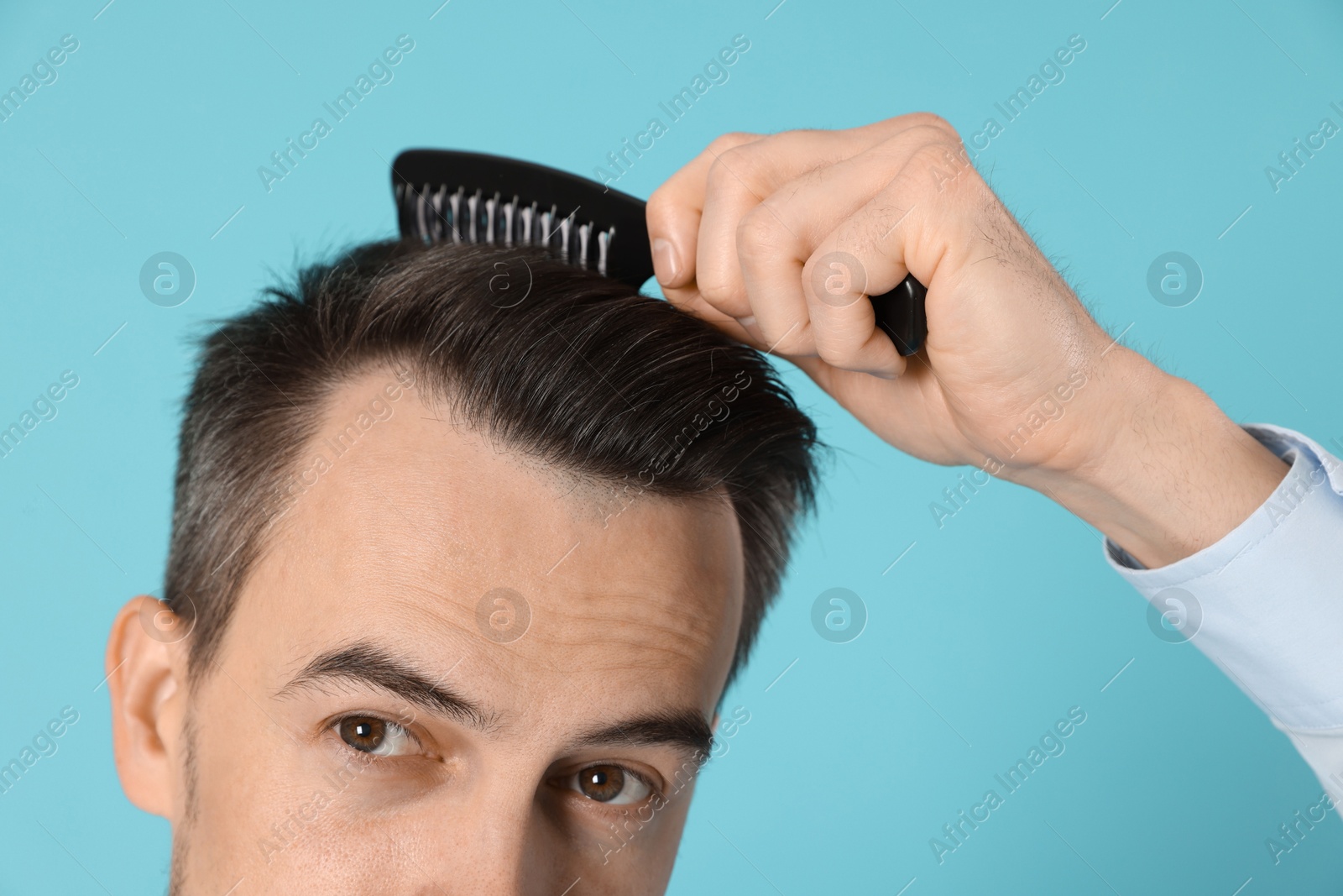 Photo of Handsome man stylish his hair with comb on light blue background, closeup