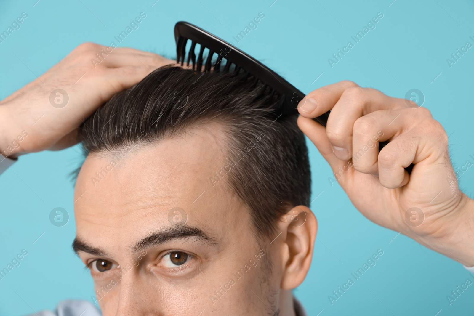 Photo of Handsome man stylish his hair with comb on light blue background, closeup