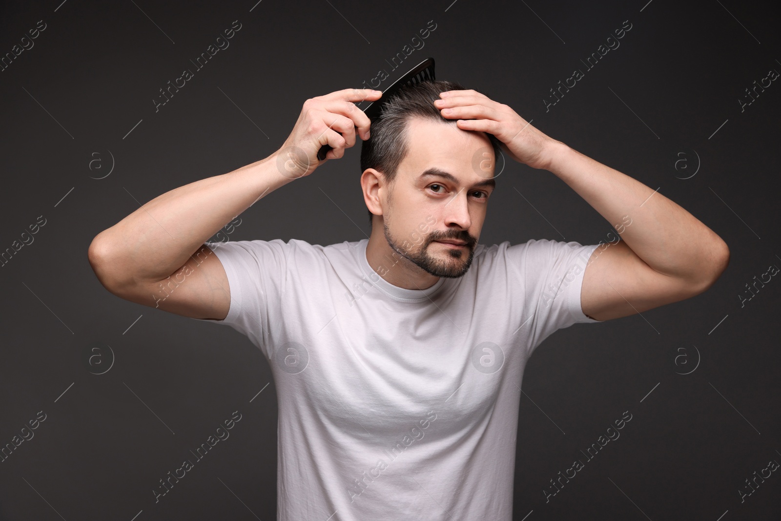 Photo of Handsome man combing his hair on dark background