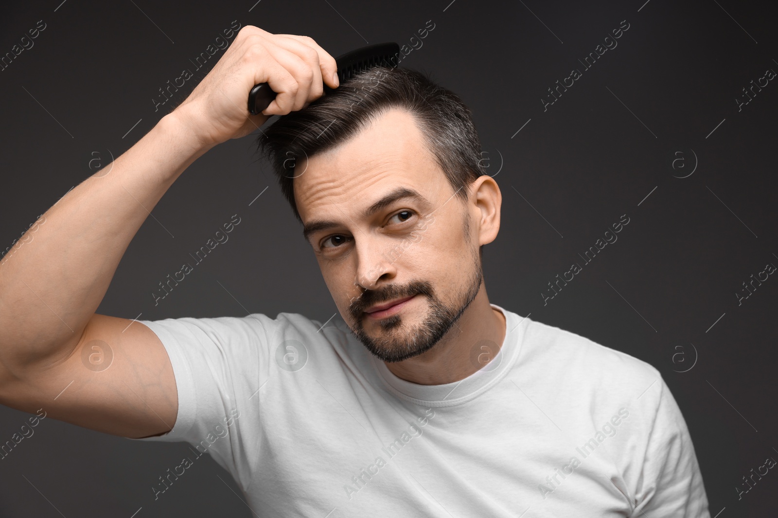 Photo of Handsome man combing his hair on dark background