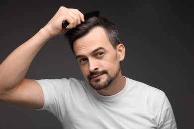 Photo of Handsome man combing his hair on dark background