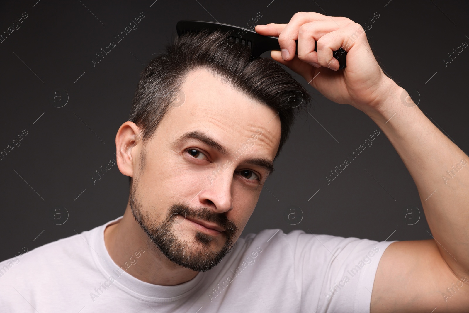 Photo of Handsome man combing his hair on dark background