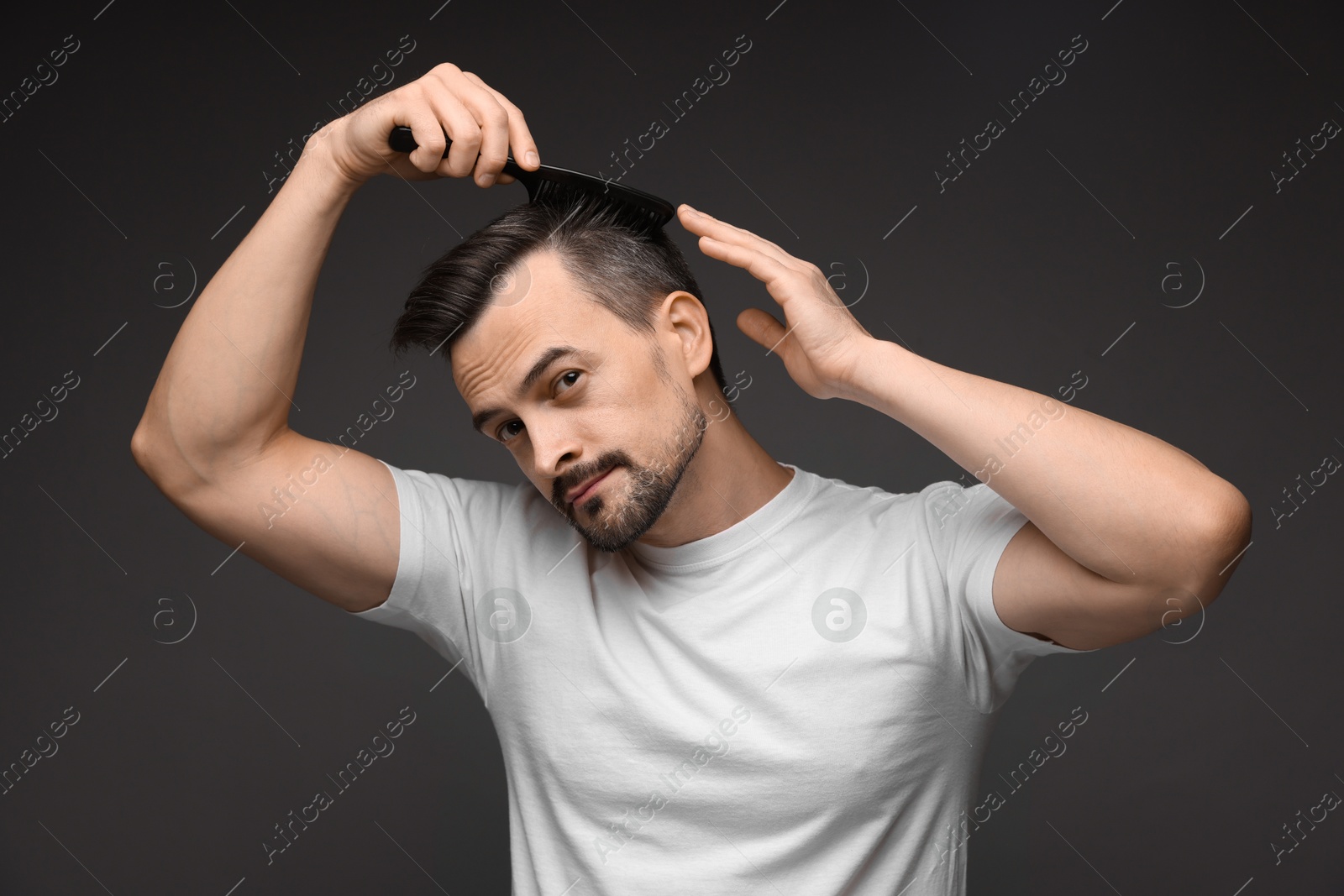 Photo of Handsome man combing his hair on dark background