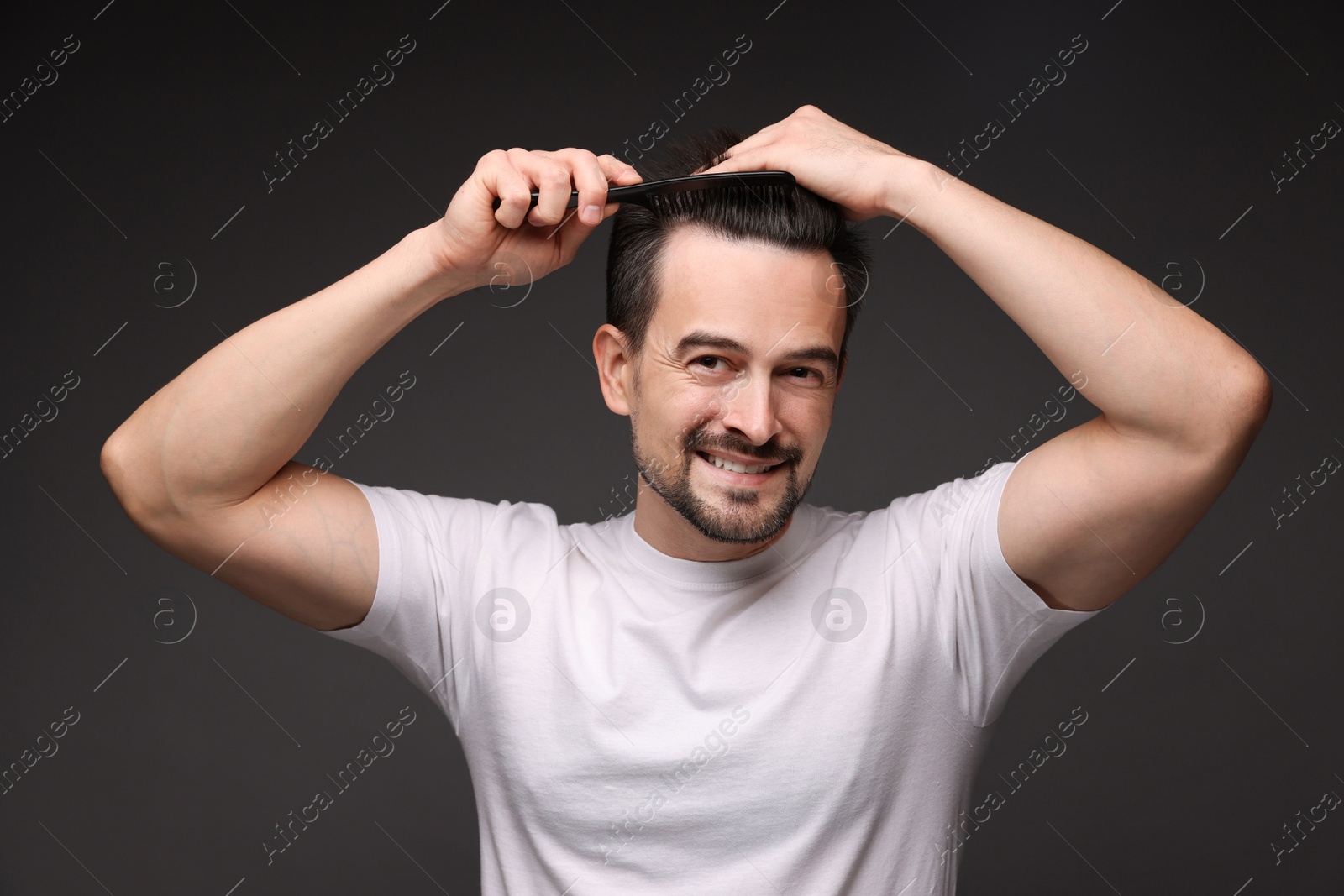 Photo of Handsome man combing his hair on dark background