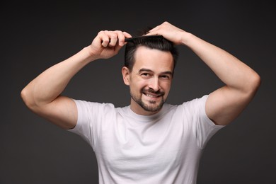 Photo of Handsome man combing his hair on dark background