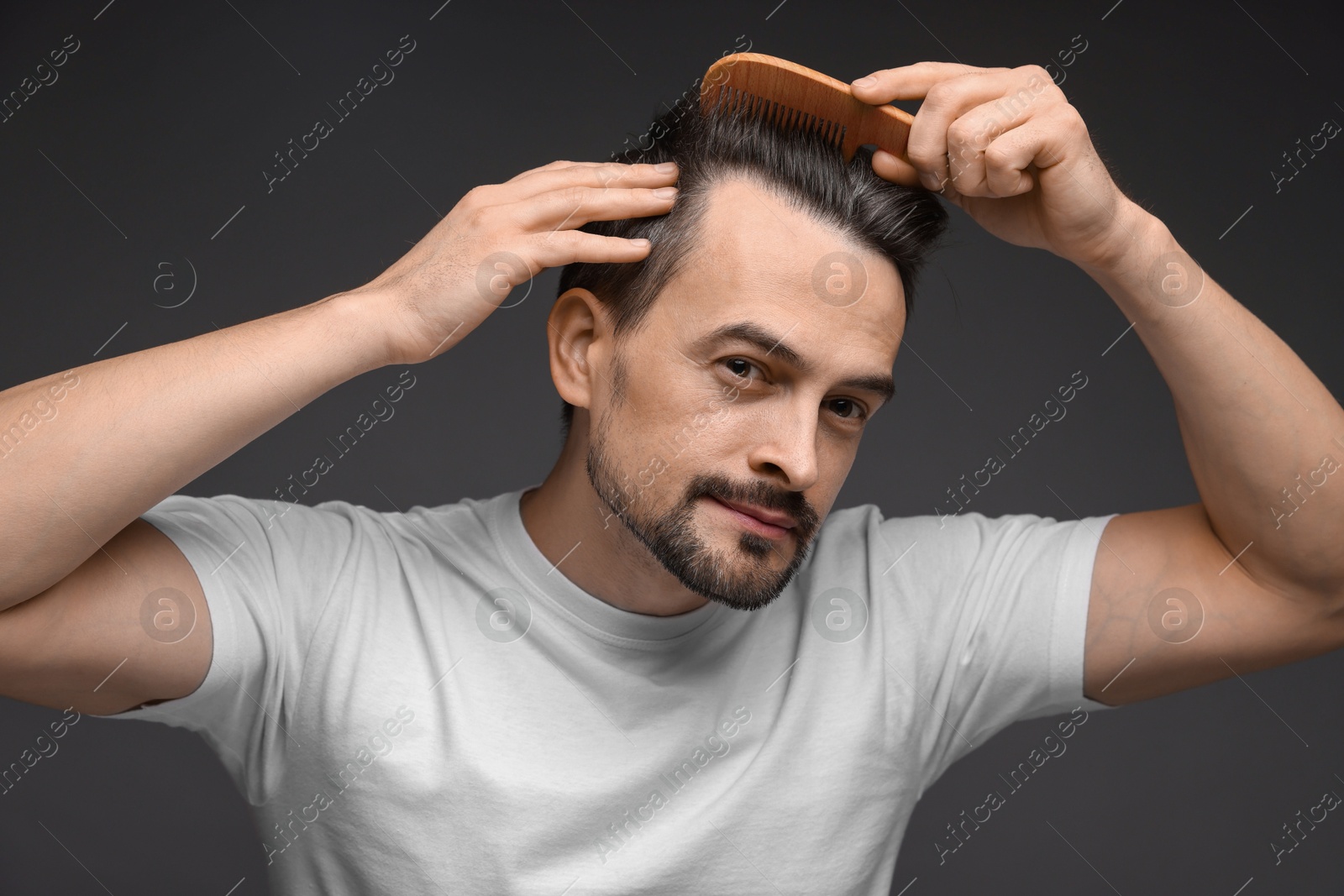 Photo of Handsome man combing his hair on dark background