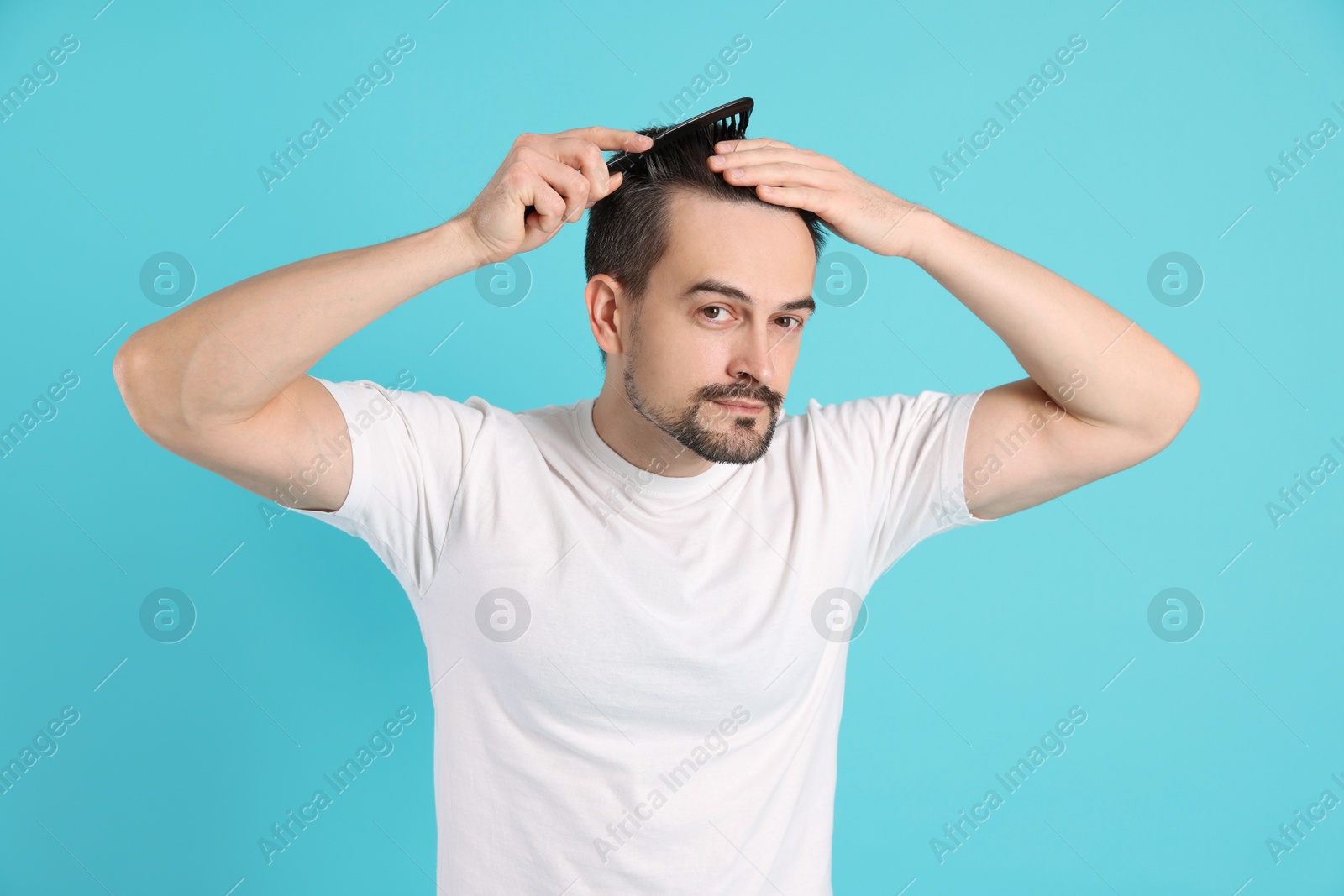 Photo of Handsome man stylish his hair with comb on light blue background