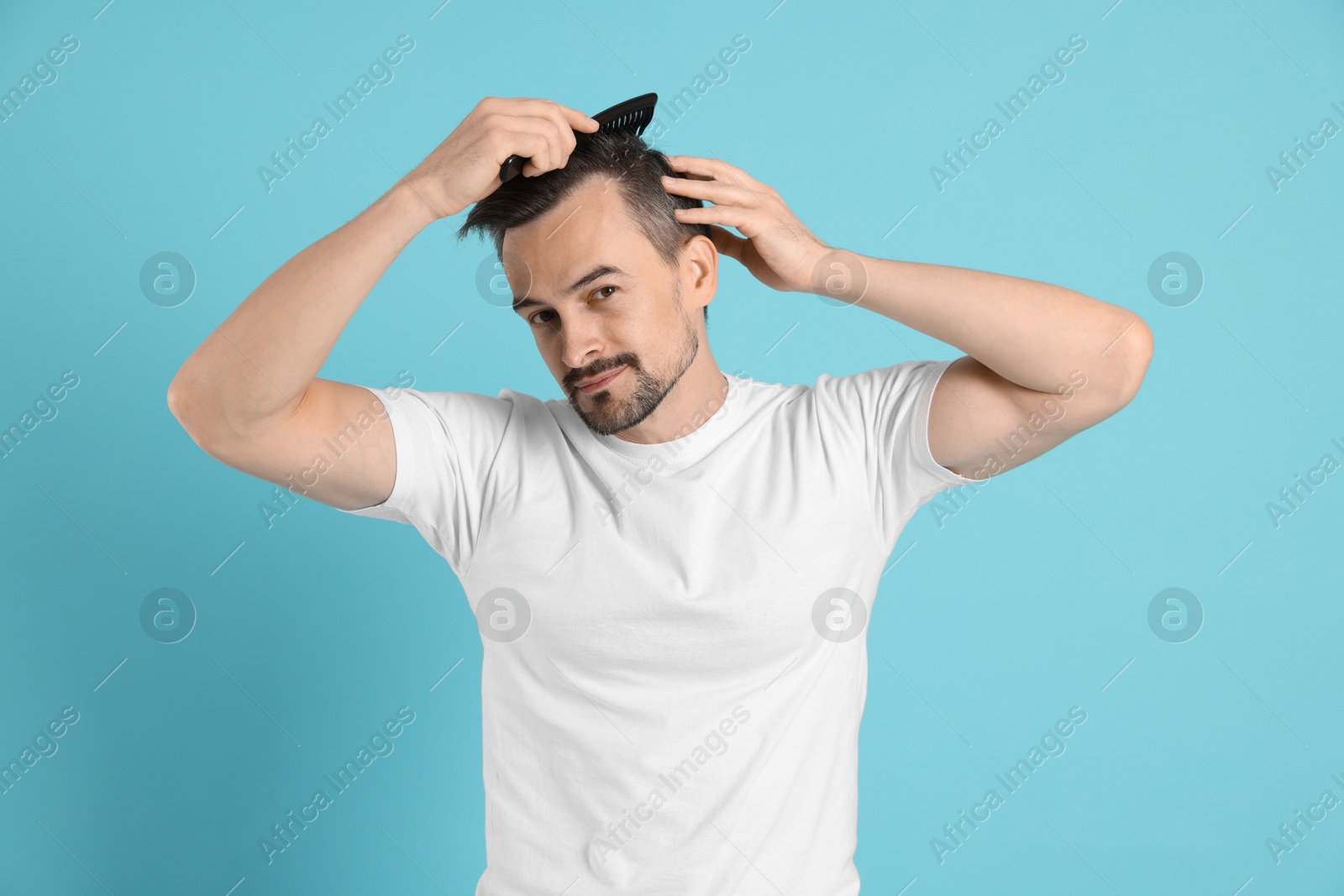 Photo of Handsome man stylish his hair with comb on light blue background