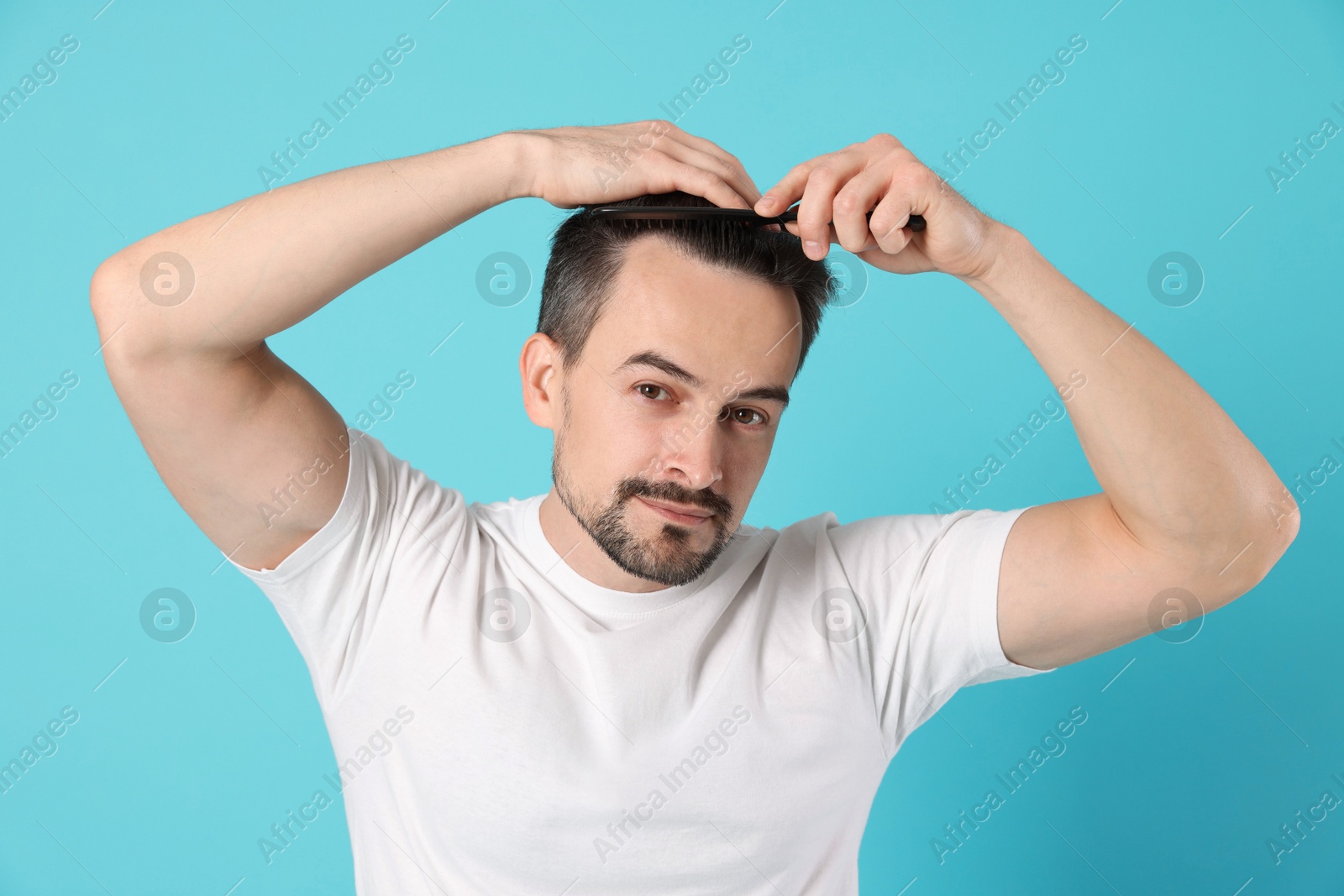 Photo of Handsome man stylish his hair with comb on light blue background