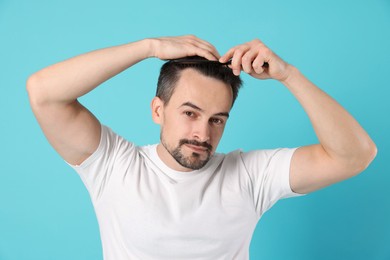 Photo of Handsome man stylish his hair with comb on light blue background