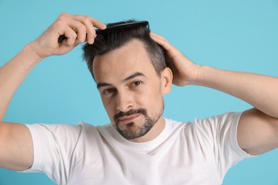 Photo of Handsome man stylish his hair with comb on light blue background