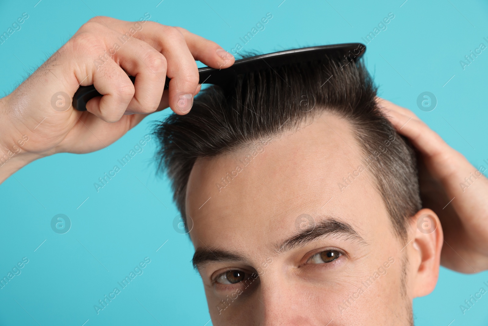 Photo of Handsome man stylish his hair with comb on light blue background, closeup