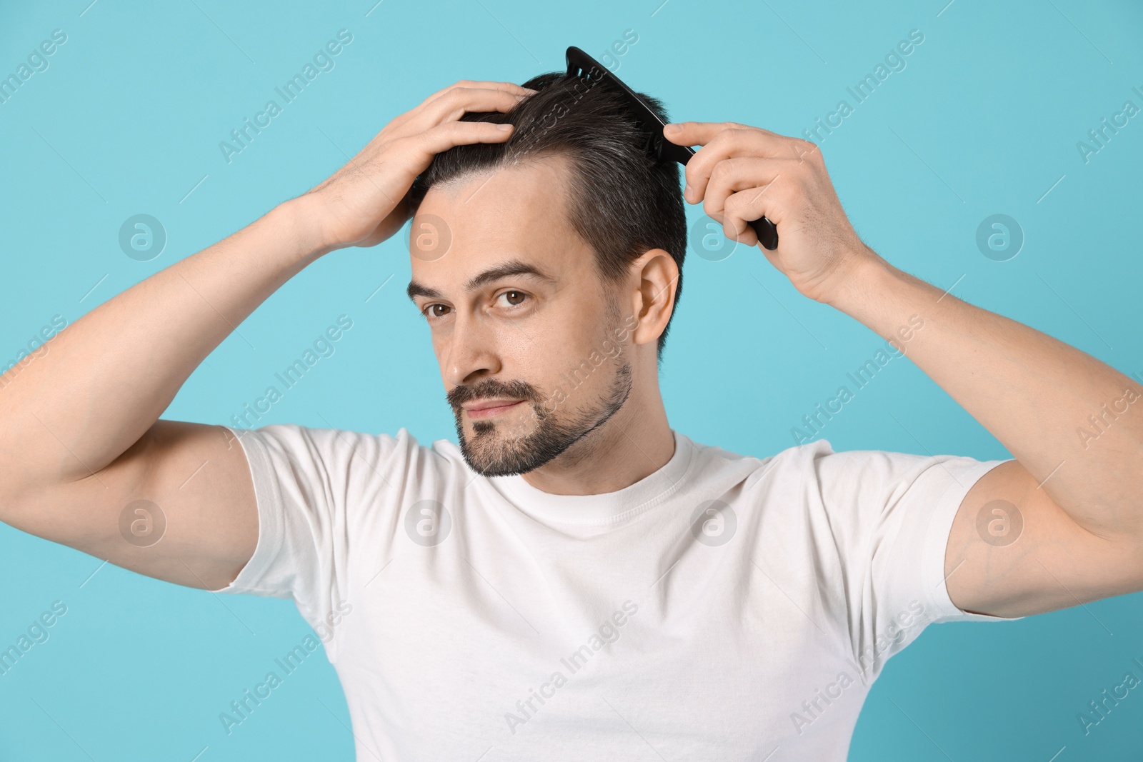 Photo of Handsome man stylish his hair with comb on light blue background