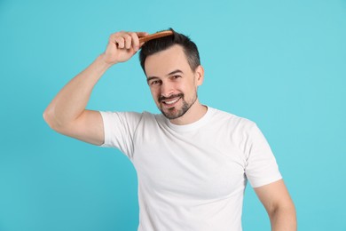 Photo of Handsome man stylish his hair with comb on light blue background