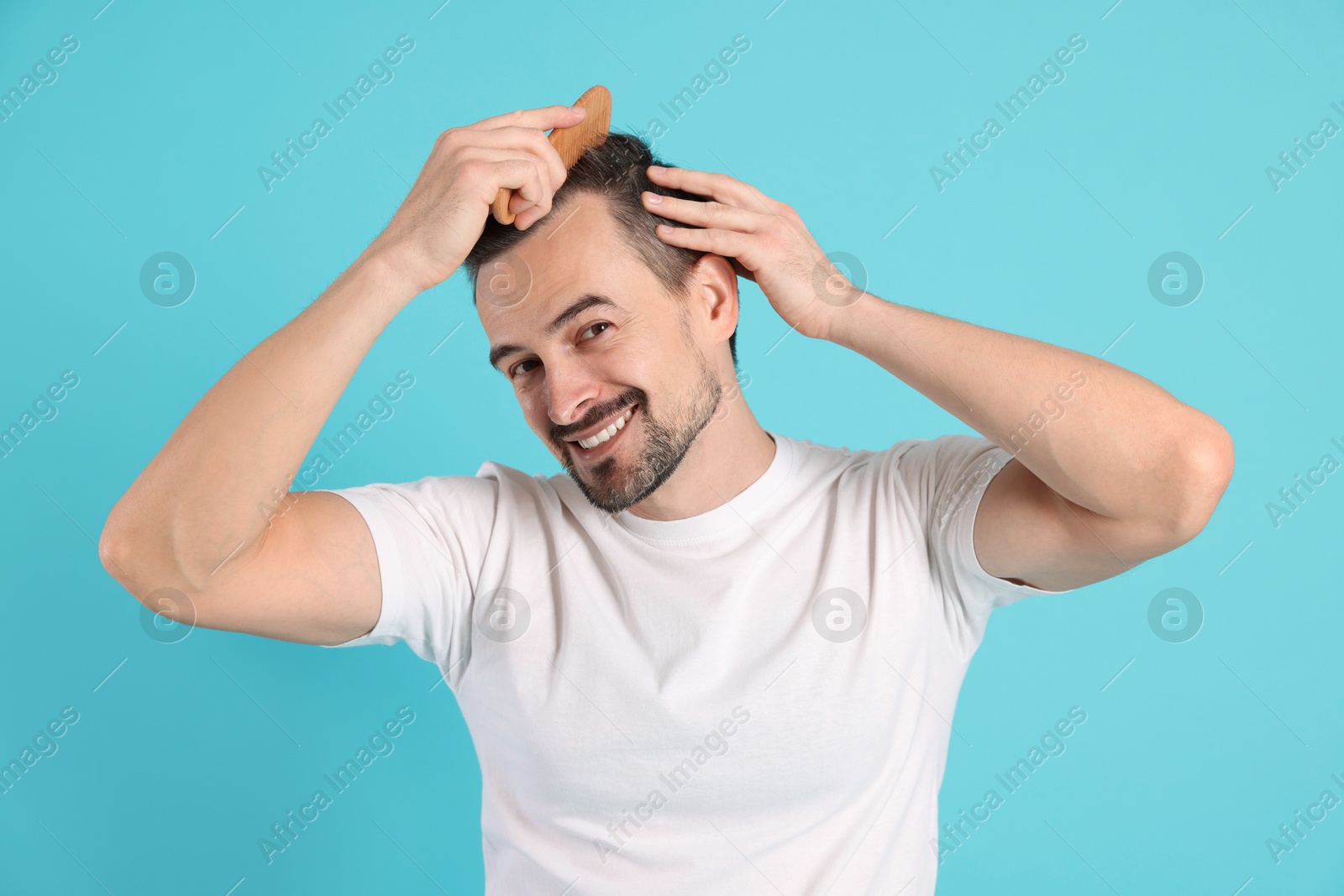 Photo of Handsome man stylish his hair with comb on light blue background