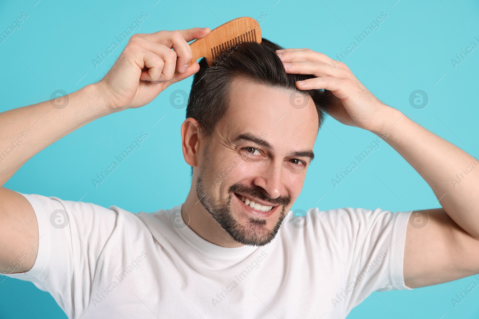 Photo of Handsome man stylish his hair with comb on light blue background