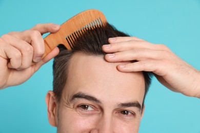 Photo of Handsome man stylish his hair with comb on light blue background, closeup