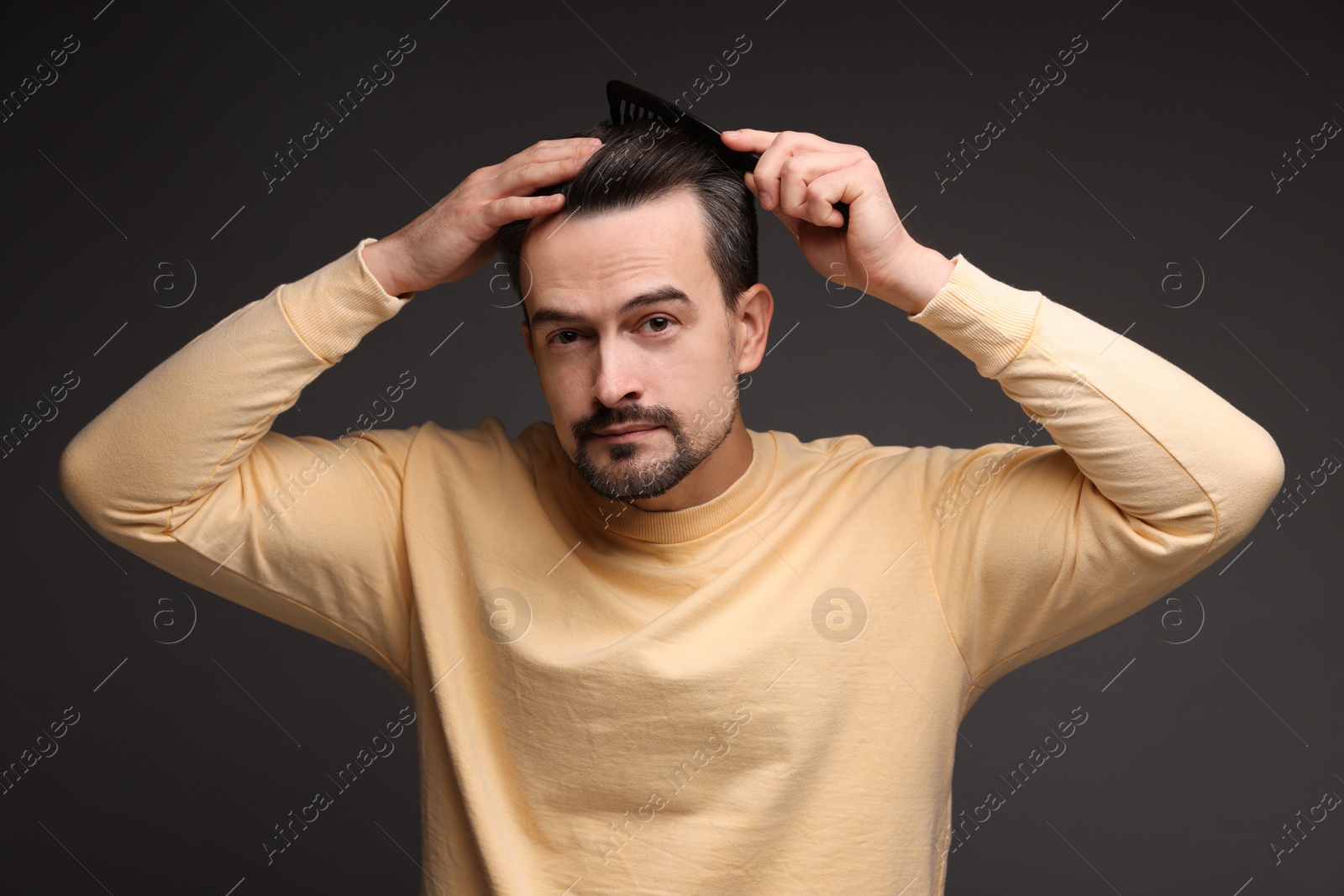 Photo of Handsome man combing his hair on dark background