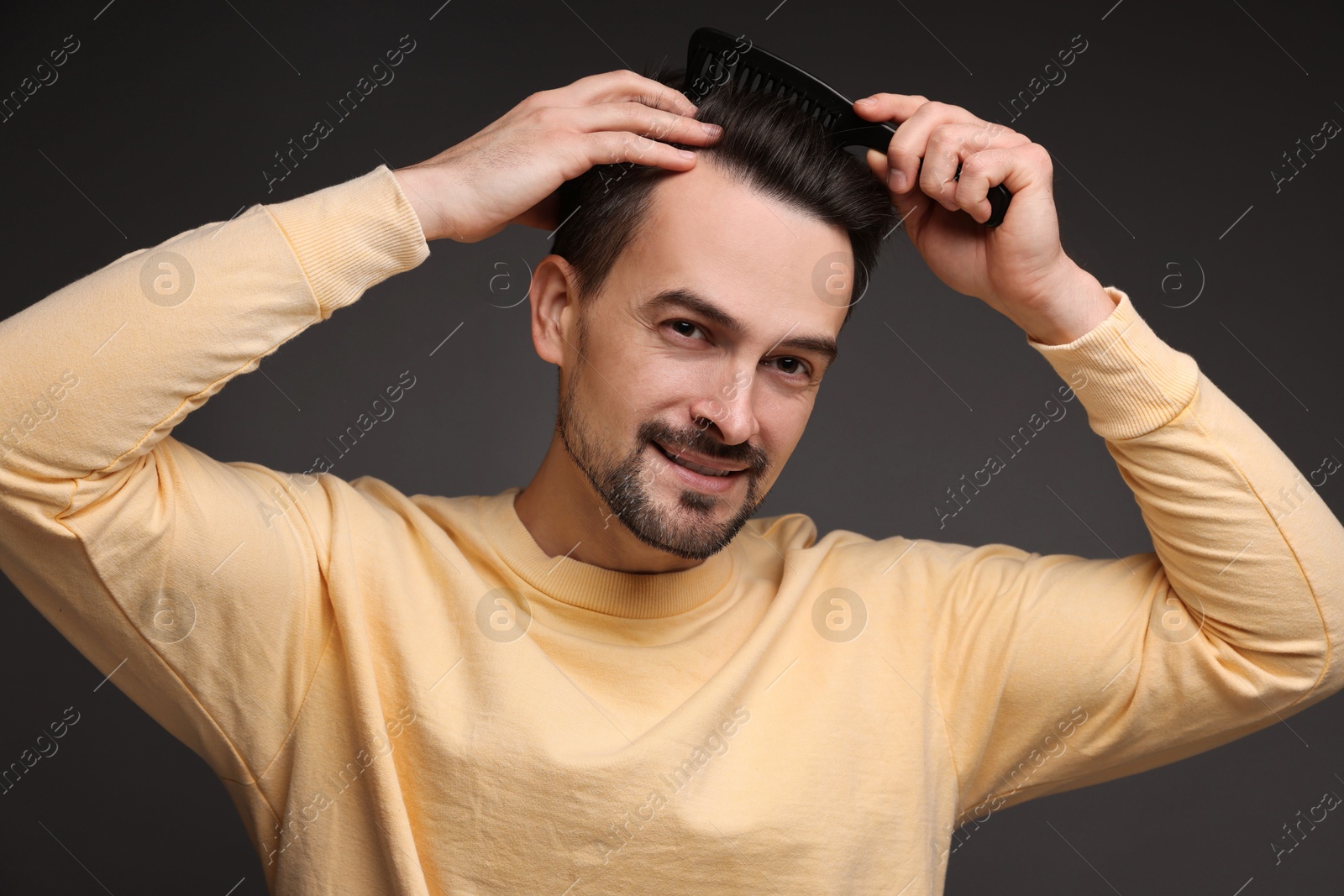 Photo of Handsome man combing his hair on dark background