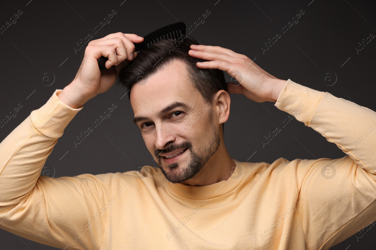 Photo of Handsome man combing his hair on dark background