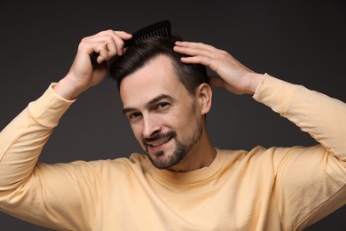 Photo of Handsome man combing his hair on dark background