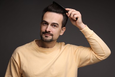 Photo of Handsome man combing his hair on dark background