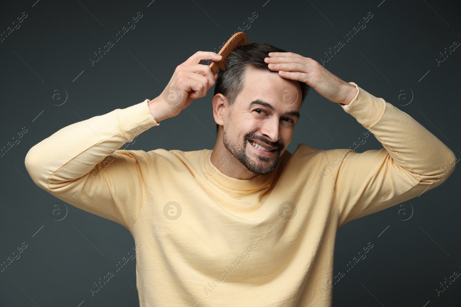 Photo of Handsome man combing his hair on dark background