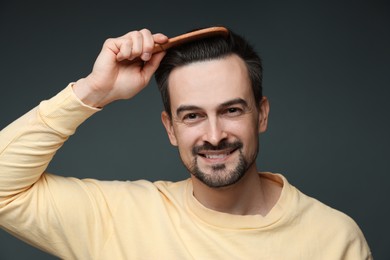 Photo of Handsome man combing his hair on dark background