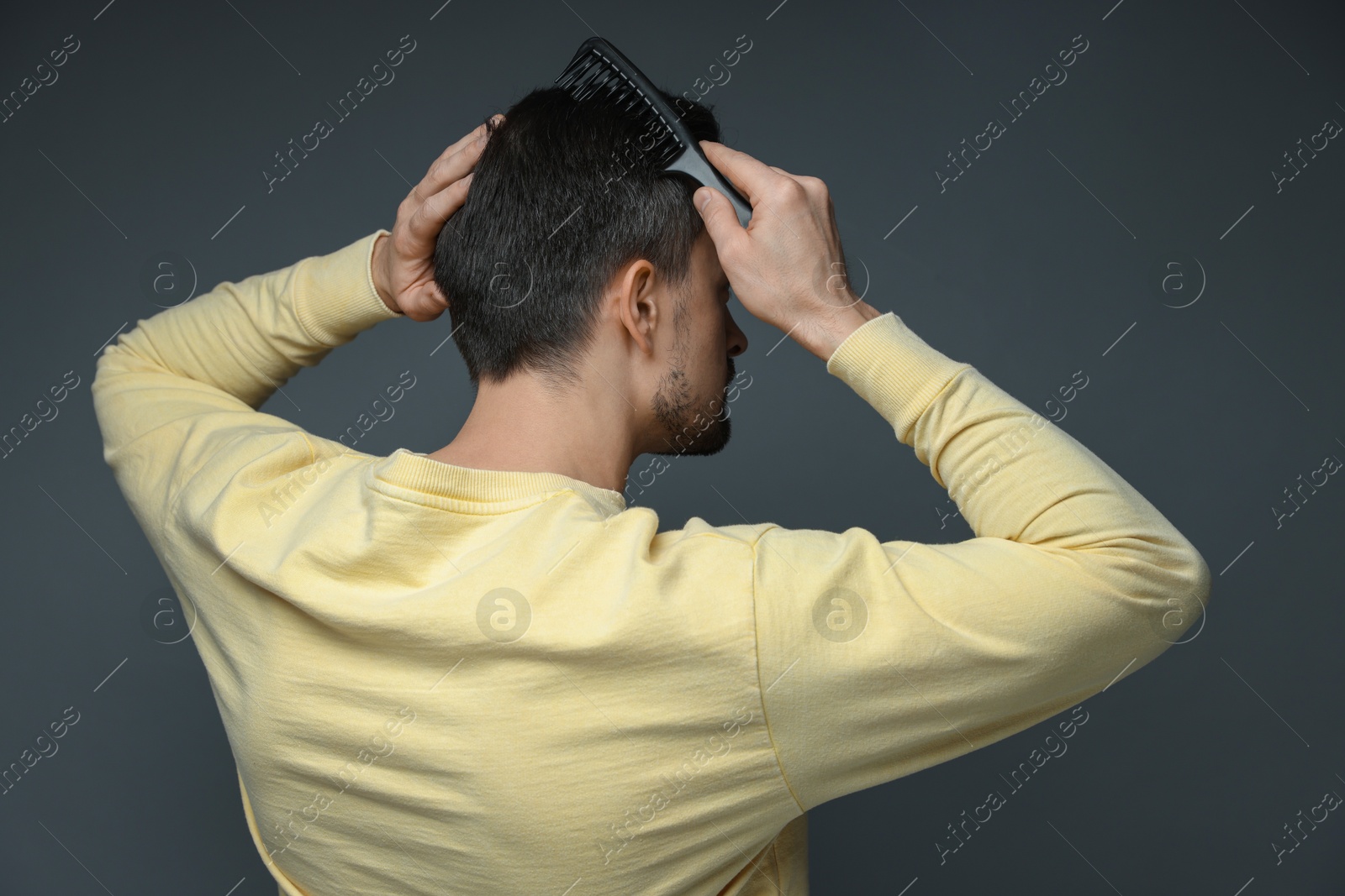 Photo of Man combing his hair on dark background, back view