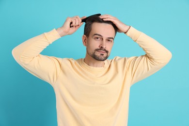 Photo of Handsome man stylish his hair with comb on light blue background