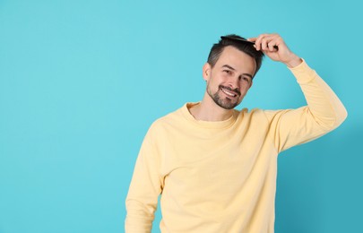 Photo of Handsome man stylish his hair with comb on light blue background