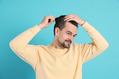 Photo of Handsome man stylish his hair with comb on light blue background