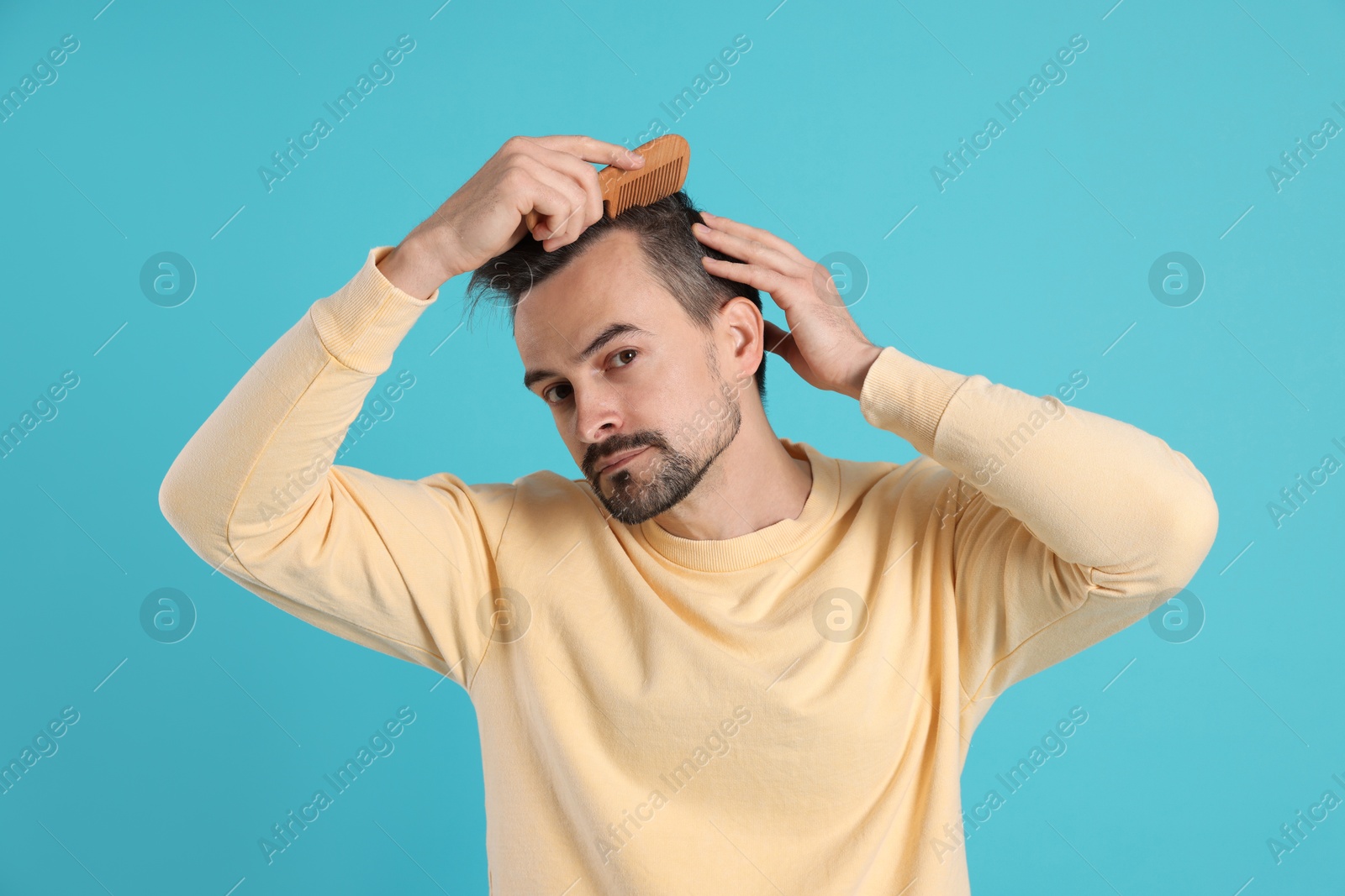 Photo of Handsome man stylish his hair with comb on light blue background