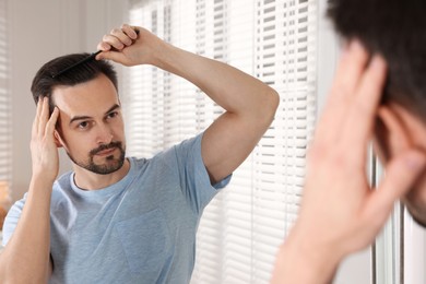 Photo of Handsome man styling his hair with comb near mirror at home