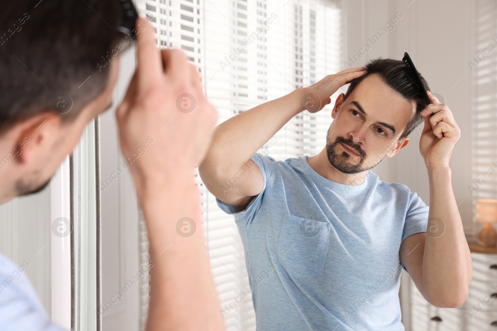 Photo of Handsome man styling his hair with comb near mirror at home